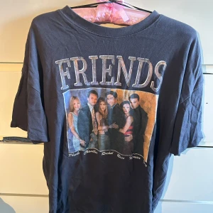 Svart Friends t-shirt från H&M - Cool svart t-shirt från H&M med stort Friends-tryck på framsidan och bild på hela gänget. Klassisk passform och rund hals. Perfekt för dig som älskar serien och vill ha en avslappnad stil.