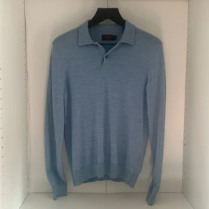 Ljusblå merinoull pikétröja Morris - Snygg ljusblå pikétröja från Morris i 100% merinoull. Tröjan har klassisk krage, knäppning framtill och långa ärmar. Perfekt för dig som gillar stilrena och bekväma plagg med premiumkänsla.