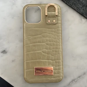 Beige croco-inspirerad mobilväska i skinn - Snygg grönt mobilskal från iDeal of Sweden med croco-mönster och gulddetaljer. Skalet har en stilren metallbricka framtill och en guldfärgad ring upptill. En liten bit har lossnat som syns på bilden och har tappat liite färg. Därav priset. Nypris 499kr❤️