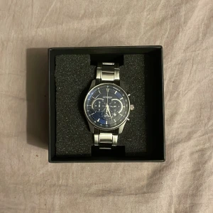 Citizen herrklocka med blå urtavla - Säljer en snygg Citizen herrklocka med blå urtavla och flera små urtavlor för extra funktioner. Klockan har ett robust armband i silverfärgat metall och klassisk rund form. Perfekt accessoar för dig som gillar stilrena detaljer och modern design.