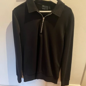 Svart långärmad tröja från ASOS - Svart långärmad tröja från ASOS DESIGN med krage och half zip-dragkedja framtill. Enkel och stilren design som passar perfekt till både jeans och chinos. Mjuk och bekväm bomullskvalitet.