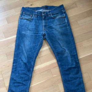 Blå jeans från Nudie Jeans - Snygga blå jeans från Nudie Jeans med klassisk femficksdesign och raka ben. Jeansen har tydliga slitningar och kontrastsömmar, samt läderpatch bak i midjan. Perfekta för en avslappnad och cool stil.