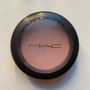 MAC Angel Matte Powder Blush - MAC Angel Matte Powder Blush i en rund svart dosa med transparent lock. Färgen är en mjuk, ljusrosa ton med matt finish. Perfekt för att ge kinderna en naturlig och fräsch look. Innehåller 6g puderrouge.