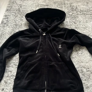 Svart velour hoodie Juicy Couture - Svart hoodie i mjuk velour från Juicy Couture med glittrande Juicy-text i strass på ryggen och liten logga fram. Långa ärmar, huva med snörning och dragkedja. Perfekt för dig som gillar klassisk Y2K-stil. Pris kan diskuteras!