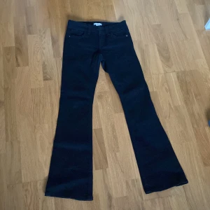Svarta bootcut jeans med fickdetaljer - Snygga svarta lowaist jeans med bootcut-modell och klassiska fickor. Byxorna har coola bakfickor med knappdetaljer och breda benslut. Knappt använda. Köpta för 500.