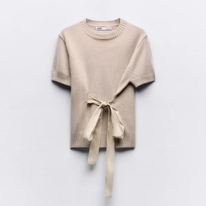 Beige stickad topp med knyt från Zara - Superfin beige stickad topp från Zara med korta ärmar och rund hals. Snygg detalj med knytband i midjan som ger en unik look. skriv om ni vill ha bild på