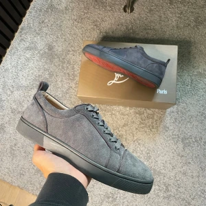 Louboutin skor  - Snygga grå sneakers från Christian Louboutin i mjuk mocka med klassisk röd sula och rund tå. Skorna har platt sula, snörning och diskreta detaljer som ger en clean look. Perfekta för dig som gillar exklusiva och stilrena sneakers.