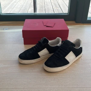 Valentino flycrews svartvita  - Svarta och vita Valentino flycrews med klassisk låg siluett. Skorna har en bred vit panel på sidan, svarta snören och detaljerade nitar på hälen. Tillverkade i mocka och skinn för en lyxig känsla. Kommer med original röd box och kort. Defekt en spik borta 