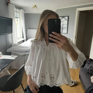 Vit blus med broderade detaljer Zara - PRISK KAN DISKUTERAS. Säljer en söt vit blus från Zara med broderade hålmönster och spets vid halsen. Blusen har knappar framtill, volangdetaljer vid axlarna och lång ärm. 