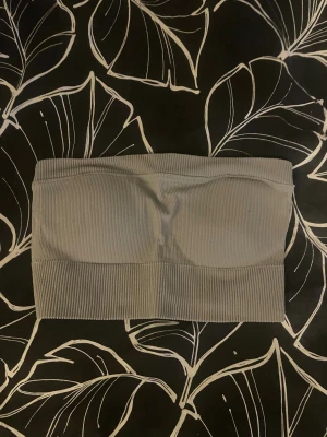 Grön ribbad bandeau tubtopp - Säljer en stilren grön bandeau tubtopp med ribbad struktur. Toppen är axelbandslös och har en bred kant nedtill för extra komfort. Perfekt att styla med höga jeans eller under en skjorta. Enkel och snygg design som funkar till många looks.