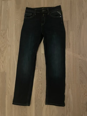 Mörkblå jeans från Replay - Snygga mörkblå jeans från Replay med klassiska kontrastsömmar och femficksdesign. Jeansen har rak passform och är tillverkade i slitstarkt bomullsjeansmaterial. Märkesdetaljer syns på fickan och bak vid linningen. Perfekta för en stilren och avslappnad look. Jag säljer dem då det är ett hål där bak som jag har sytt men jag tycker inte det blev så bra, om man har dem på sig så ser man inte hålet så tydligt det är bara om man kollar mycket på de, man kanske kan rita över med en mörkblå penna