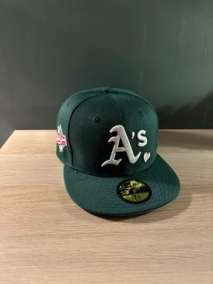 Flatted keps - Unik snygg grön Oakland Athletics keps från New Era med broderad A's-logga i vitt och en liten baseball-detalj på framsidan. Platt skärm med grå undersida och klassisk passform. Använd en gång men det är inte min stil så därför säljer jag den. Pris kan diskuteras vid snabb affär!