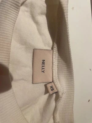 Vit topp med knyt från Nelly - Säljer en vit topp från Nelly i bomull med halvlånga ärmar och snygg öppen rygg med breda band som knyts i en rosett bak. Toppen har en clean look och passar perfekt till allt. Modellen är slim och ger en fräsch vibe.