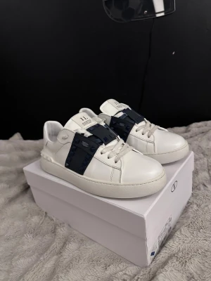 Valentino opens Rockstud 11 sneakers vit/blå - Tja säljer feta Valentino skor. Dem är så i bra skick med några små defekter. På bild 5 så är det en spik/knapp som har ramlat av. Dem kommer med extra skosnören, verifikations kort och två olika påsar. Det finns ett serienummer på insidan så om ni vill ha det fråga privat. Om ni har några andra frågor så är det bara att skicka om ni vill ha bättre bilder eller om det finns någon defekt på ett ställe. Nypris är runt 7000kr men mitt pris är 2999kr. Jag tar emot prisförslag