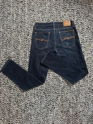 Nudie jeans 31/32 - Ett par supersnygga Nudie Jeans med en snygg wash och bra passform!😄Nudie jeansen är i modellen Tight Long John. Blir perfekta för höst och vinter med den mörkare washen. Litet slitage på ena bakfickan(syns på bild) men inget man tänker på i verkligheten. Annars är dem nästintill nya!🤩 Nypris: ca 1400kr. Mitt pris 499kr, men kom gärna med prisförslag då priset inte är hugget i sten!