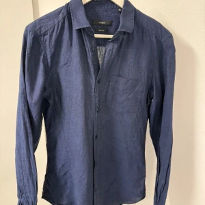 Blå linneskjorta Z Zegna Drop 8 Fit - Snygg blå skjorta från Z Zegna i Drop 8 Fit med klassisk krage och bröstficka. Tillverkad i lätt och luftig linne, perfekt för dig som gillar stilren och enkel design. Långärmad modell med knappar hela vägen framtill.