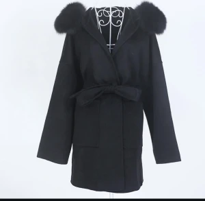 Svart kappa med päls och bälte - Stilren svart kappa med huva och stora pälsdetaljer på axlarna. Kappan har knytbälte i midjan, stora fickor framtill och raka ärmar. Perfekt för dig som vill ha en trendig och mysig look under kallare dagar.