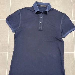 Marinblå pikétröja från Ermenegildo Zegna - Snygg marinblå pikétröja från Ermenegildo Zegna i storlek XS men sitter som S. Tröjan har klassisk krage, tre knappar framtill och korta ärmar. Materialet är mjukt och andas, perfekt för dig som gillar stilren och enkel design.