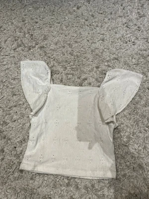 Vit blus med broderade detaljer Kappahl - Supersöt vit blus från Kappahl i storlek 146/152. Toppen har broderade hålmönster och korta, voluminösa ärmar som ger en romantisk vibe. Perfekt till jeans eller kjol för en fräsch look. Materialet känns lätt och luftigt.