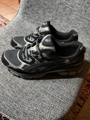 Asics skor nyc gel svarta  - Säljer ett par svarta och grå Asics sneakers med mesh och syntetpaneler. Skorna har snörning, rund tå och en rejäl platt sula. Perfekta för dig som gillar sportig stil och vill ha bekväma skor till vardagen. Klassisk Asics-logga på tungan och sidan.