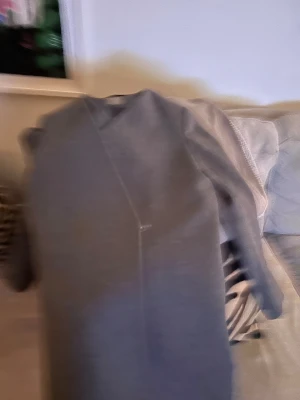 Grå kappa från COS, storlek 38 - Säljer en stilren grå kappa från COS i storlek 38. Kappan har en minimalistisk design med rak passform och lång ärm. Sparsamt använd och i bra skick. Snyggt fodrad insida och diskret v-ringad hals. Enkelt att matcha med din garderob.