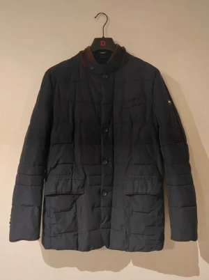 Mörkblå quiltad jacka från Park Lane - Snygg mörkblå quiltad jacka från Park Lane med bruna manchesterdetaljer på kragen. Jackan har knäppning med stora knappar, två rejäla fickor framtill och en klassisk, stilren look. Perfekt för dig som gillar tidlös design.