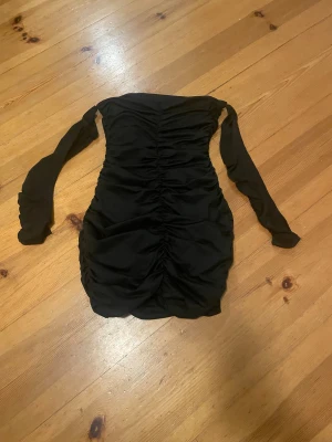 Svart ruched kortklänning från SHEIN - Snygg svart kortklänning från SHEIN i storlek XS. Klänningen har långärmade ärmar och är designad med ruched detaljer längs hela framsidan för en cool och trendig look. Materialet är mjukt och följsamt, perfekt för dig som gillar att sticka ut.