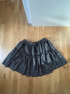 Svart prickig kortkjol  - Supersöt svart kortkjol från SHEIN med vita prickar och volangdetaljer. Kjolen har resår i midjan och är gjord i ett lätt, flowy material som känns luftigt