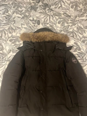 Svart dunjacka från Canada Goose - Säljer en svart Canada Goose dunjacka med pälskantad huva och klassisk patch  då den enda dragkedjan har gått sönder och inte kostar så mycket att köpa en ny och sätta på men pris går att diskutera mvh robin 