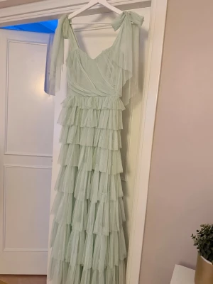 Lace & Beads MAXI klänning  - Drömmig ljusgrön långklänning i flera lager mesh med volanger hela vägen ner. Axelbanden knyts med stora rosetter och klänningen har omlottkänsla upptill. Perfekt för dig som älskar det lilla extra!