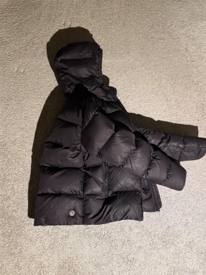 Svart pufferjacka från Colmar - Säljer en svart pufferjacka från Colmar med huva och dragkedja. Jackan har en oversized look, stora fickor och klassisk Colmar-logga på bröstet. Perfekt för kalla dagar och riktigt skön att bära. Passar dig som vill ha en varm och stilren vinterjacka.