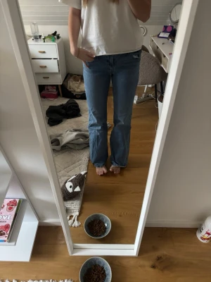 Blå bootcut jeans - Säljer ett par klassiska blå jeans med bootcut-modell. Jeansen har en rak passform upptill och blir vidare nedtill. Tillverkade i jeansmaterial med en ljusblå tvätt och råa kanter vid benslut. Perfekta för en avslappnad och trendig look.