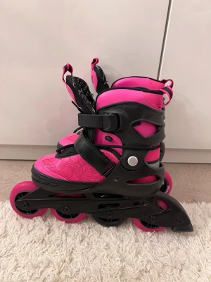 Rosa och svarta rull skor  - Säljer ett par snygga inlines från Coolkick i rosa och svart med blommigt mönster. De har justerbar storlek, snörning och spänne för extra support. Hjul i rosa med svart detalj, 80mm. 