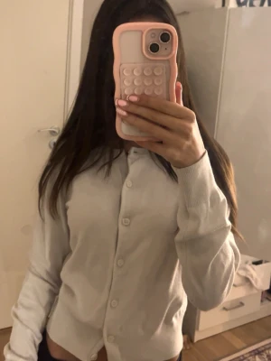 Vit kofta från H&M i bomull XS - Säljer en enkel och stilren vit kofta från H&M i storlek XS. Koftan har långa ärmar, ribbade muddar och knäpps med knappar framtill. Perfekt att slänga över en topp för en clean look.