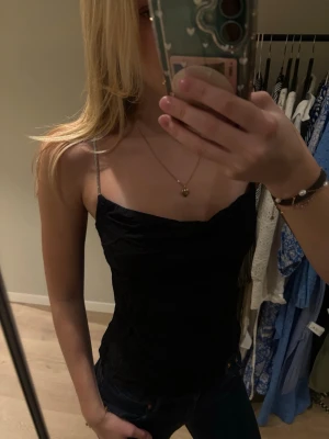 Svart linnetopp från H&M med glittriga band - Säljer en svart linnetopp från H&M i storlek XS. Toppen har tunna glittriga axelband och en lätt draperad urringning. Perfekt att styla med jeans eller kjol för en snygg look. Skrynklig men går att fixa 