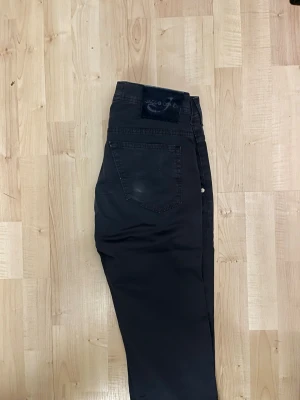 Svarta Jacob Cohën jeans, storlek 31 - Säljer ett par svarta jeans från Jacob Cohën i storlek 31. Byxorna har klassisk femficksdesign, raka ben och snygga silverfärgade nitar. Materialet känns mjukt och exklusivt, perfekt för dig som gillar stilrena och tidlösa plagg.