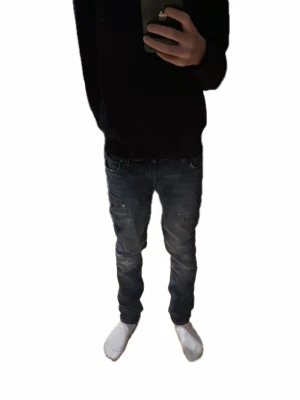 Slim fit jeans från Jack & Jones - Säljer ett par mörkblå slim fit jeans från Jack & Jones med snygga slitningar och klassiska fem fickor. Jeansen har normal passform och är tillverkade i mjukt bomullsmaterial med lite stretch för extra komfort. Perfekt för dig som gillar en modern och stilren look.