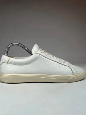 Vita Saint Laurent sneakers i skinn - Klassiska vita sneakers från Saint Laurent i mjukt skinn med diskret logga på sidan. Modellen har rund tå, platt sula och snörning framtill. Snygg minimalistisk design som passar till allt. Sulan är i en ljusbeige ton som ger en clean look.