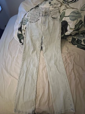 Ljusblå jeans med tryck från F3 Sister - Säljer ett par ljusblå jeans från F3 Sister i storlek XXS. Jeansen har coolt svart tryck med texten 'BUY ME A TICKET TO...' fram och 'LOS ANGELES' bak på fickorna. Modellen är raka och högmidjade med klassisk femficksdesign och knappgylf.💗
