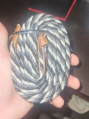 Randig flätad bälte med läderdetaljer - Tjenare säljer nu ett flätat bäldte då det bara är ivägen och behöver göra mig av med en del kläder och smycken.Säljer ett snyggt randigt bälte i svart och vitt med bruna läderdetaljer och silverfärgat spänne. Bältet är flätat och har en cool, ungdomlig vibe som passar till jeans eller chinos. Perfekt accessoar för att lyfta din outfit.