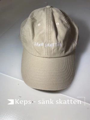 Sänk skatten keps - Beige keps där det står sänk skatten. Går att justera där bak