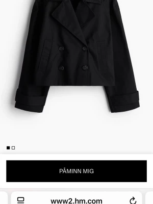 Svart croppad trenchcoat från H&M - Säljer en svart croppad skepparkavaj från H&M med dubbelknäppning och bred krage. Jackan har långa ärmar och raka fickor framtill. Perfekt för dig som vill ha en stilren och trendig look. Slutsåld!!!