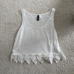 Vit croppad linnetopp från H&M Divided - Säljer en vit croppad linnetopp från H&M Divided i storlek XS. Toppen har breda axelband, rund halsringning och en snygg spetskant med virkade detaljer längst ner. Perfekt till sommaren och enkel att matcha med jeans eller kjol.