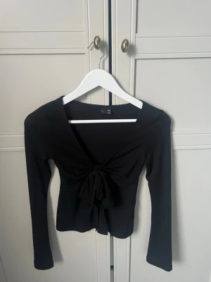 Svart knytblus från Gina Tricot - Säljer en svart långärmad topp från Gina Tricot i storlek XXS. Toppen har en djup v-ringning och snygg knytning framtill.
