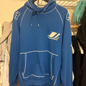 J.Lindeberg Concorde hoodie - Säljer en blå hoodie från J.Lindeberg med vita tryck och loggor på bröst och rygg. Bra skick endast använd fåtal gånger.