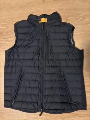 Svart dunväst från Parajumpers S - Säljer en svart dunväst från Parajumpers i storlek S. Västen har quiltad design, hög krage med gul detalj och dragkedja framtill. Två sidofickor med dragkedja och en bröstficka. Superlätt och perfekt för lager-på-lager under kyliga dagar.
