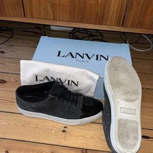 Lanvin svarta sneakers med mocka - Lanvin sneakers i svart mocka med blank svart tå och vita platta sulor. Klassisk låg modell med snörning och rund tå. Snygg kontrast mellan matt mocka och glansig tå, perfekt för dig som gillar stilrena och exklusiva sneakers.inner sulan är 29,5cm