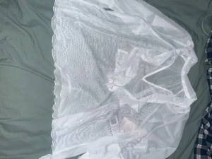 Vit mesh kortklänning med volang - Säljer en vit kortklänning i mesh med transparent tyg och volangdetaljer längs kanterna. Klänningen har omlottband för knytning i midjan och ger en luftig och trendig look. Perfekt för dig som gillar att sticka ut med en unik och modern stil.