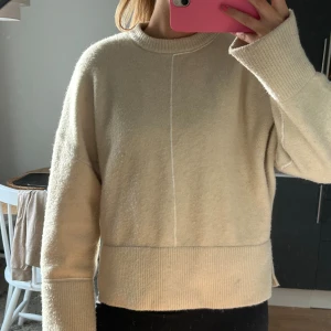 Beige stickad tröja från Zara - Säljer en beige stickad tröja från Zara i storlek M. Tröjan har en rund halsringning, ribbade muddar och en snygg söm framtill. 