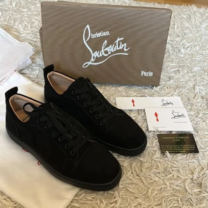 Christian Louboutins- Dior - Säljer ett par helt nya, exklusiva Christian Louboutin sneakers i storlek 43. Skorna är i svart mocka med den ikoniska röda sulan och klassisk snörning, perfekt för både vardag och fest. De kommer med originalförpackning, dustbags och alla intakta originalkort, vilket gör detta till ett oslagbart erbjudande för den som söker kvalitet och stil. Ett unikt tillfälle att äga ett par lyxiga och aldrig använda Louboutin-skor i nyskick, som garanterat kommer att höja din garderob. 